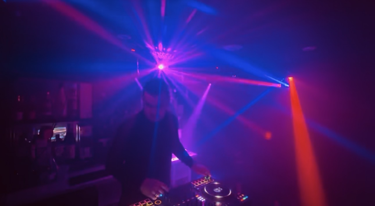 A DFRACTD DJ mixing under vivid blue and orange stage lighting